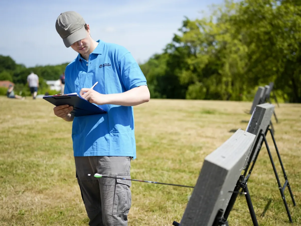 mand skriver paa clipboard ved bueskydningsbane