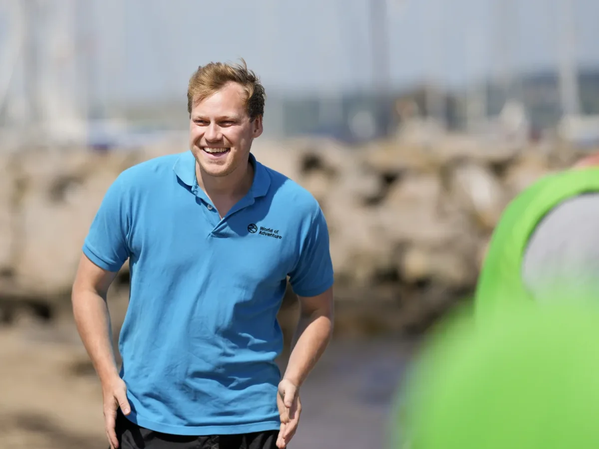 mand smiler ved havn med groen vest i baggrunden