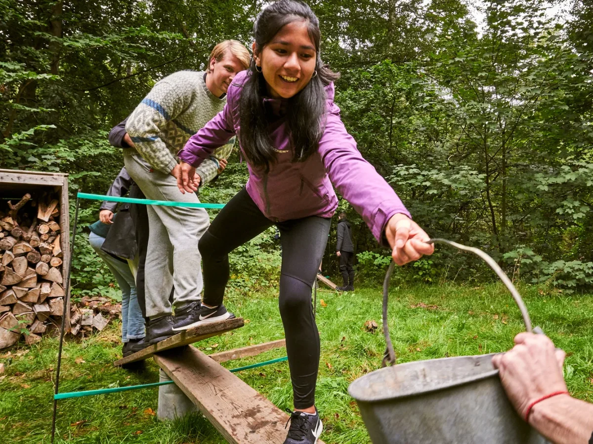 dsc00383 kvinde i lilla jakke balancerer paa bjaelke med spand