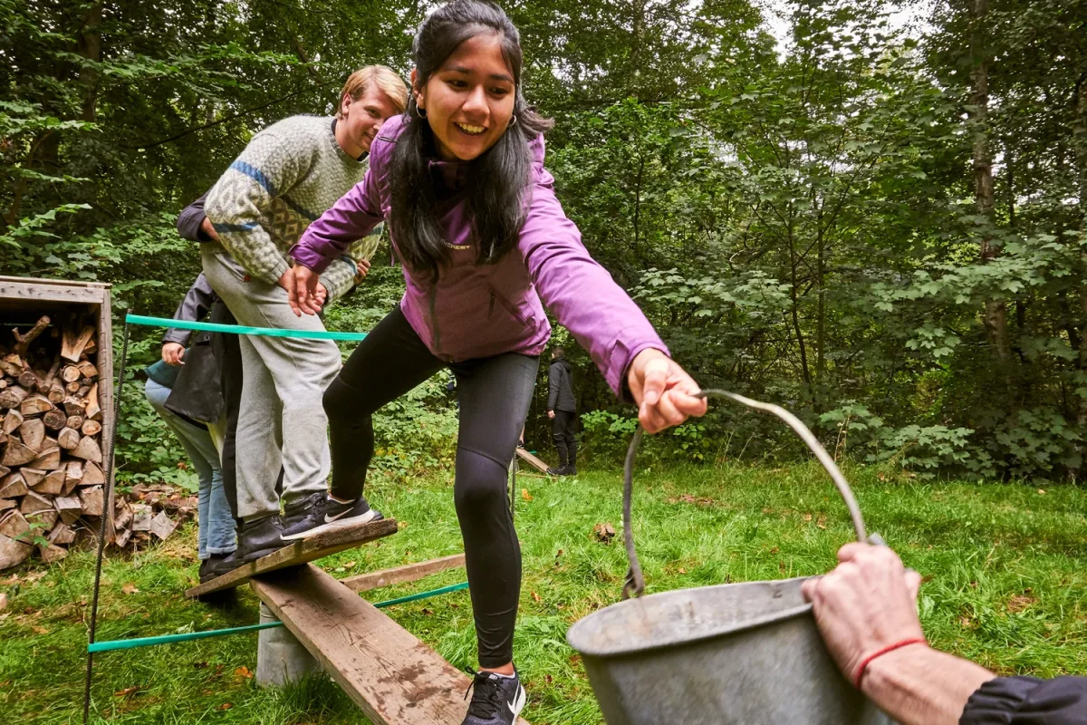 dsc00383 kvinde i lilla jakke balancerer paa bjaelke med spand