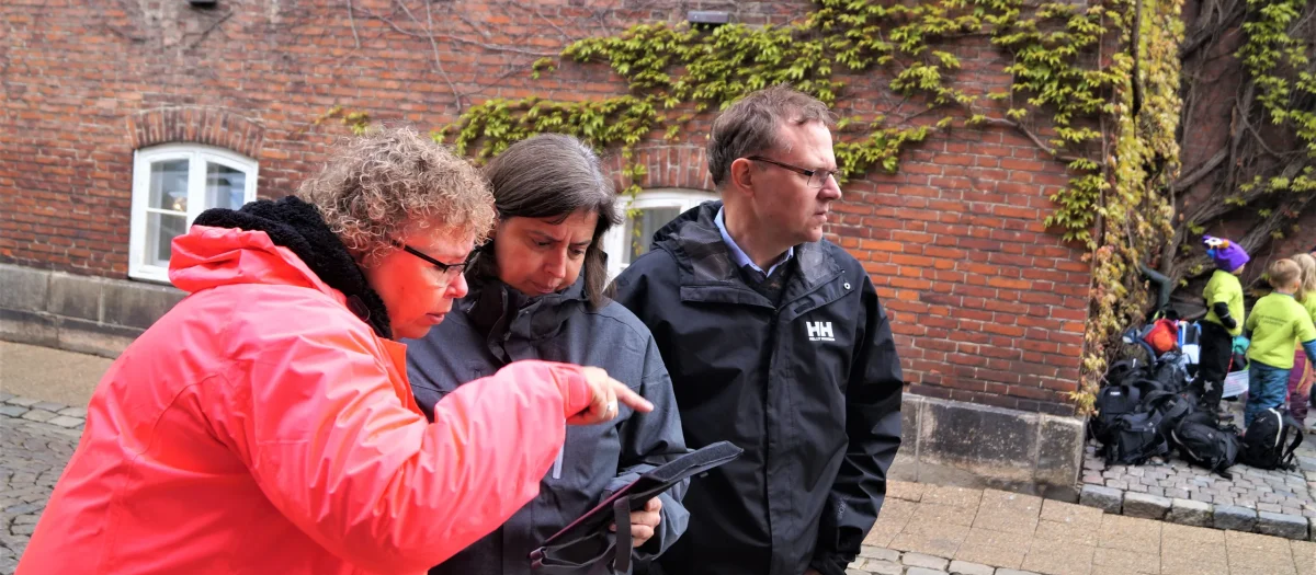 Deltagere i byeventyr står sammen og studerer kort eller navigation på byens gade