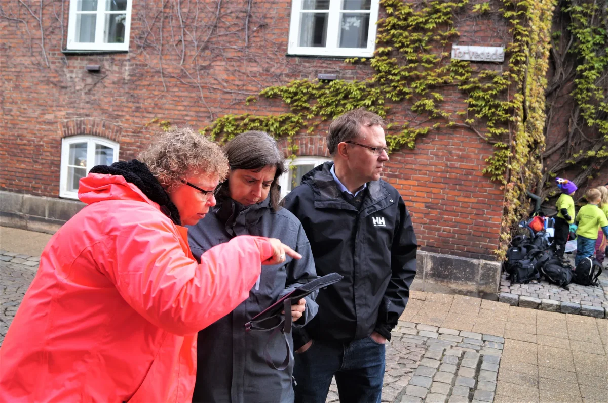 Deltagere i byeventyr står sammen og studerer kort eller navigation på byens gade