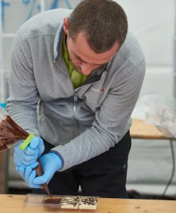 Deltagere i chokolade workshop dekorerer chokoladestykker med præcision under teambuilding aktivitet