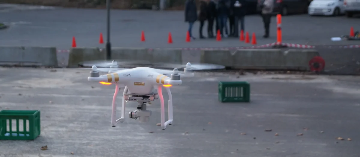 Hvid drone flyver over asfalt under teambuilding aktivitet med deltagere samlet i baggrunden
