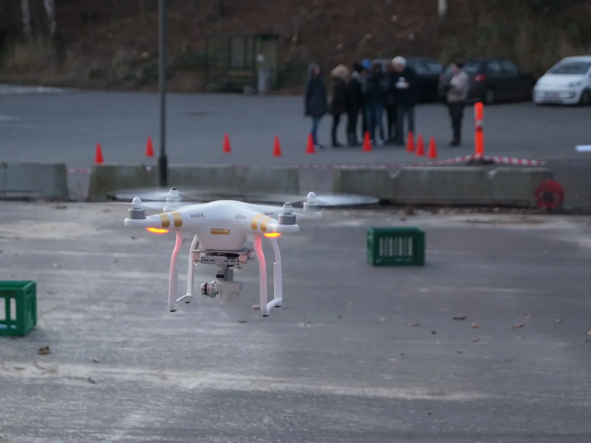 Hvid drone flyver over asfalt under teambuilding aktivitet med deltagere samlet i baggrunden