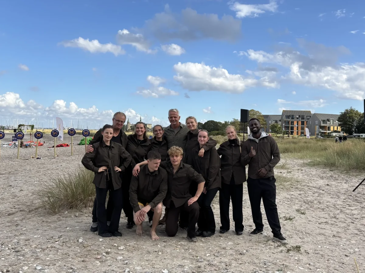 Expedition Robinson Kjelberg deltagere poserer til gruppefoto på sandstrand under blå himmel.