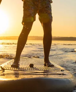 To personer står på paddleboards i vandet ved solnedgang med gylden belysning.
