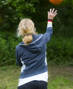 Deltagere spiller basketball udendørs under WOA Olympics med en kvinde der kaster bolden mod kurven.