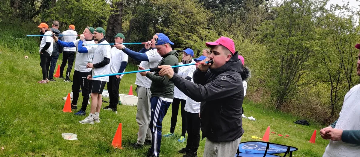 Deltagere i Woa Olympics samles på græsplæne med udstyr til udendørs konkurrenceaktiviteter.